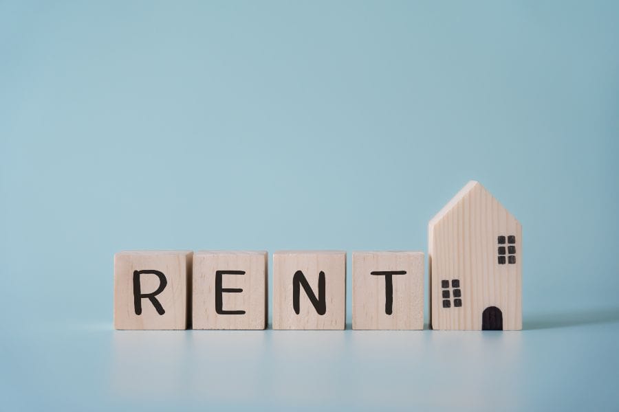 Wooden blocks spelling rent beside a small house model on blue background.